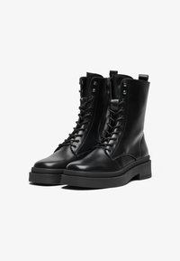 Botas de tornozelo em pele preta com atacadores na frente, fecho lateral e sola de borracha robusta com um design minimalista e acabamento mate.