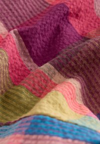 Textilná tkanina s farebnými štvorcami v ružovej, fialovej, zelenej a modrej farbe. Textúrovaný povrch s rôznymi vzormi a vyvýšenými tkaninami.