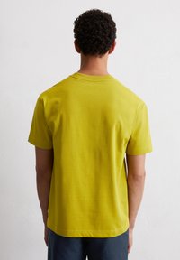 Żółta koszulka z krótkim rękawem, wykonana z miękkiej bawełny, z okrągłym dekoltem i luźnym krojem. Gładka faktura z minimalnymi detalami szwów.