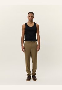 Black sleeveless tank top paired with tan pleated trousers. Brown lace-up shoes complete the outfit. Neutral backdrop.
