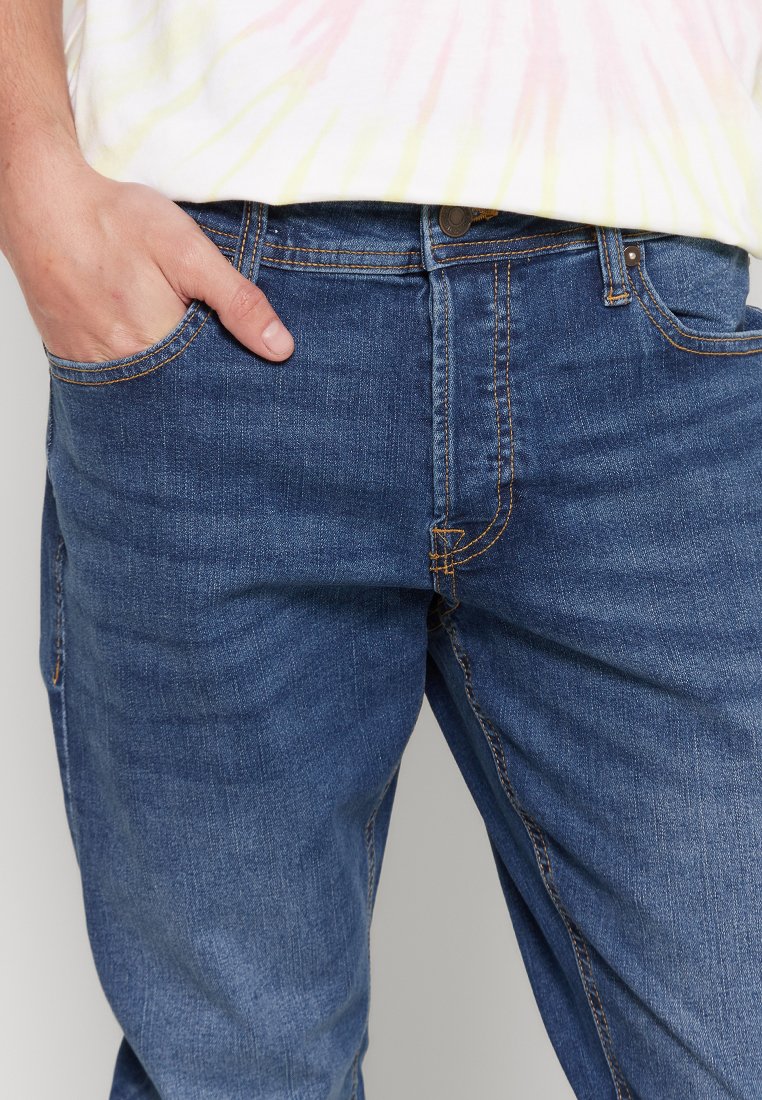 Vaqueros de denim azul con un corte recto, que cuentan con costuras naranjas, bolsillos frontales y un cierre de botón metálico. Textura suave y diseño casual.