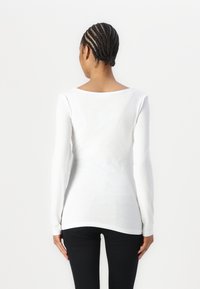 Witte langemouwen top met een ronde hals, een strakke pasvorm en een zachte textuur, gecombineerd met donkere slim-fit broek.