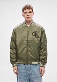 Õlilisroheline bomber-jakk satiinkangast, esil lukuga, soonikkoes mansettidega ja rinnale tikitud tekstuurse "CK" logoga.