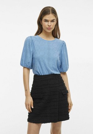Lichtblauwe blouse met een oogjesontwerp en pofmouwen, gecombineerd met een zwarte rok van textuur met gelaagd stoffen en voorzakken.