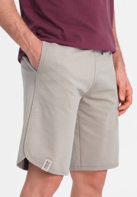 Pantalones cortos de algodón gris con un diseño sin costuras, bolsillos laterales y un pequeño acento de etiqueta en el dobladillo. Textura fuerte y suave.