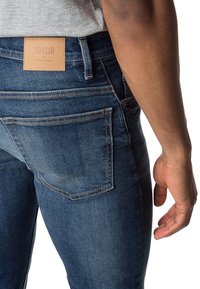 Modré džíny z denimu se rovnými nohavicemi, s koženou nášivkou na pase a klasickým pětikusovým designem kapsiček.