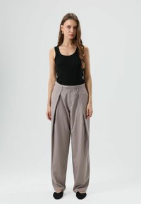 Zwart geribd tanktop gecombineerd met lichtgrijze wijd uitlopende broek met hoge taille, plooien en een tailleband met sluiting. Zwarte platte schoenen maken de outfit compleet.