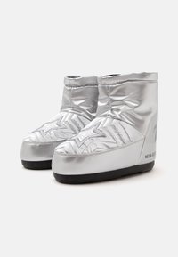 Par de botas de invierno acolchadas plateadas con costuras en forma de estrella y suelas negras, altura hasta el tobillo, con la marca "Moon Boot" en el lateral.