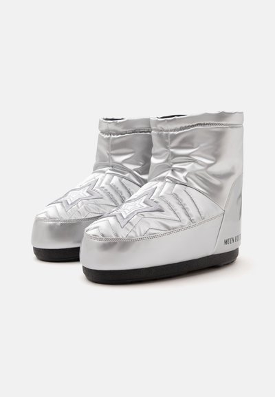 Paire de bottes d'hiver matelassées argentées avec couture en forme d’étoile et semelles noires, hauteur cheville, estampillées "Moon Boot" sur le côté.