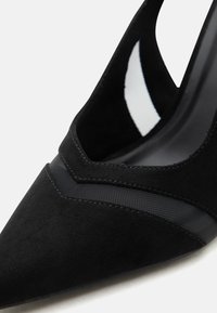 Μαύρη γόβα με μυτερή μύτη, κατασκευασμένη από σουέντ και δίχτυ, με λεπτομερείς ραφές κατά μήκος του άνω άκρου.