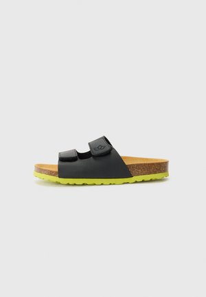 Black slide sandals with two adjustable Velcro straps, cork footbed, and a bright green rubber sole with a textured grip.
