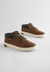 Brązowe skórzane buty typu high-top z szarym materiałowym kołnierzem, białą podeszwą środkową i gumową podeszwą o teksturowanej powierzchni. Posiadają metalowe oczka i sznurówki.