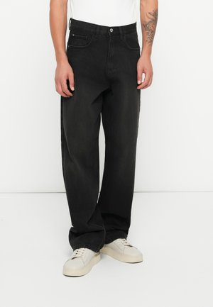 Svarte denimbukser med rett passform, med knappelukking, fem lommer og en lett falming i teksturen. Brukt med lyse sko.