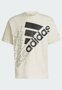 Camiseta de algodón color crema con un gran logo negro de Adidas y elementos de diseño geométrico impresos en diagonal en la parte frontal.