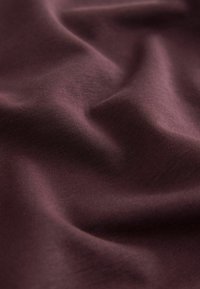Bordó anyag sima textúrával, finom ráncokkal és hajtásokkal, kiemelve a nyújthatóságát és esését. Enyhe fényesség látható.