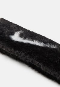 Fascia de pelúcia preta com um detalhe branco, suave e fofinho, em forma de uma letra ou símbolo estilizado. Design texturizado, espesso e peludo.