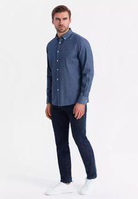 Marinemarineblauwe overhemd met een stippenpatroon; katoenmateriaal; lange mouwen; gecombineerd met donkere jeans en witte sneakers.