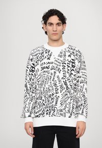 White sweatshirt featuring black graphic text in varying fonts, with a crew neck and ribbed cuffs. Casual fit and soft texture.