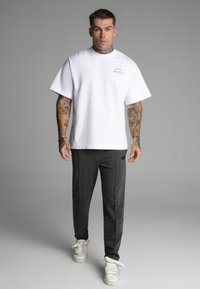 White cotton t-shirt with a round neck, paired with dark gray pinstriped trousers and white sneakers with a textured sole.