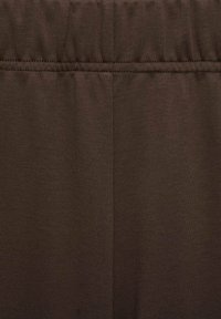 Bruine rekbare stof, gladde textuur, met een elastische tailleband en een subtiele stiknaad. Voornaamste solide kleur zonder patronen.