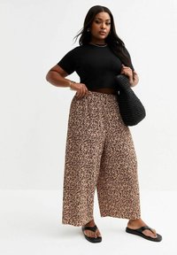 Zwarte cropped t-shirt, wijde dierprintbroek in beige en bruin, textuur zwart geweven tas en zwarte slippers.