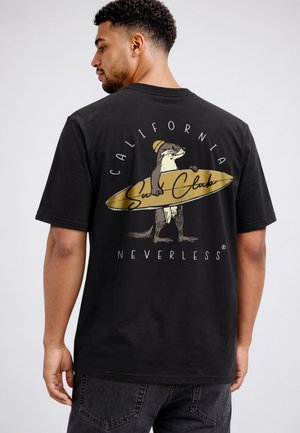 Mann trägt schwarzes T-Shirt, zeigt Rücken-Grafik eines Otters mit Surfbrett und Text „California Surf Club Nevertheless.“
