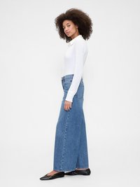 Top bianco a maniche lunghe abbinato a jeans in denim blu a vita alta e gamba larga. Ballerine nere e dettagli di cucitura minimali sui jeans.