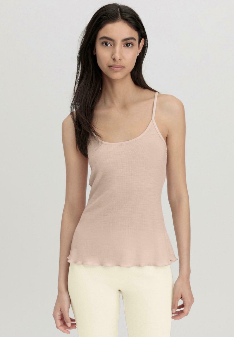 Light pink ribbed tank top with thin adjustable straps and a curved hem, paired with light off-white leggings.