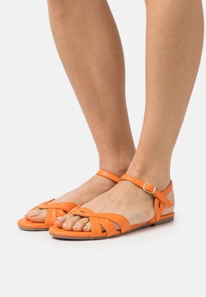 Sandales en cuir orange avec des brides au niveau de la cheville, présentant un design entrecroisé et des semelles plates. Texture lisse et style ouvert au niveau des orteils.
