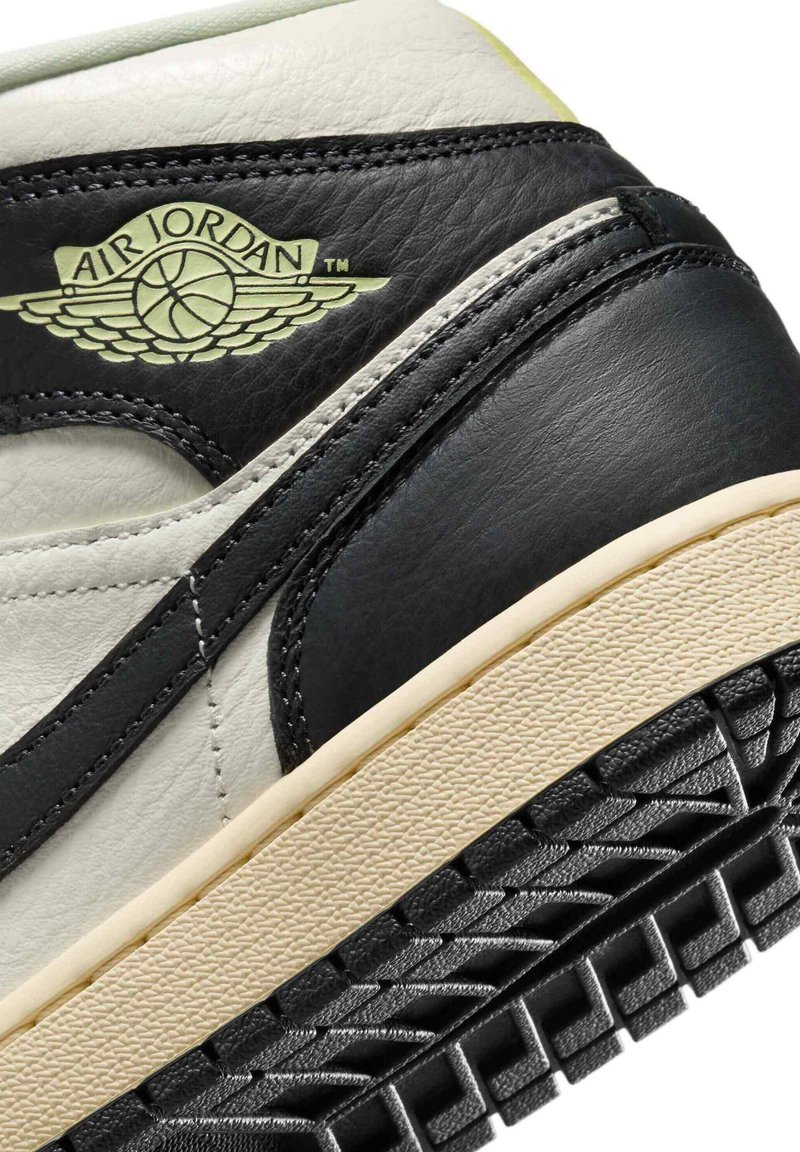 Zapatilla de cuero negra y crema con suela texturizada. Presenta el logo de Air Jordan en relieve y costuras en contraste en la parte superior.