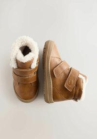 Braune Leder-Kinderstiefel mit weißem Fleece-Futter und doppeltem Klettverschluss vor einem hellen neutralen Hintergrund.