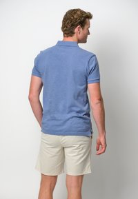 Blå kortärmad polo tröja gjord av lätt tyg, med krage och sidofickor, tillsammans med ljusa beige shorts.