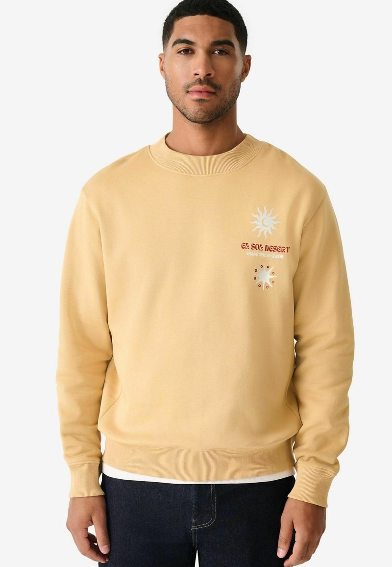 Gul sweatshirt med ribbet halsudskæring og manchetter. Har et solgrafik og teksten "El Sol Desert" på brystet, med en glat tekstur.