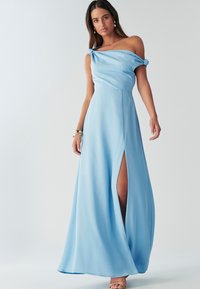 Taevasinist värvi maksikleit paljastavate õlgadega, millel on sõlmega varrukad ja reie kõrgune lõhik, valmistatud siledast ja voogavast kangast.