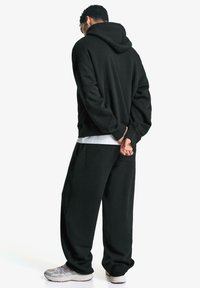 Zwarte hoodie en bijpassende broek in een ontspannen pasvorm, gemaakt van zacht materiaal met een gestructureerd oppervlak. Voorzien van een grote capuchon en zijzakken.