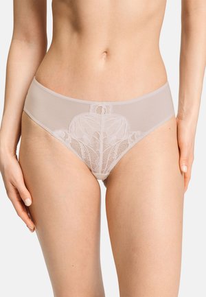 Frau trägt beige Spitzenunterwäsche mit Blumenmustern, dargestellt von der Taille bis zu den oberen Oberschenkeln vor einem einfarbigen Hintergrund.