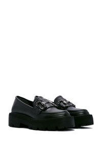 Mocassins en cuir noir avec une semelle plateforme épaisse, dotés d'un accent décoratif en chaîne argentée à l'avant et d'une texture lisse.