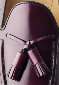 Bordeaux leren schoen met een ronde vorm, decoratieve kwastjes en contrasterende stiksels langs de rand. Gladde afwerking met een glanzende textuur.