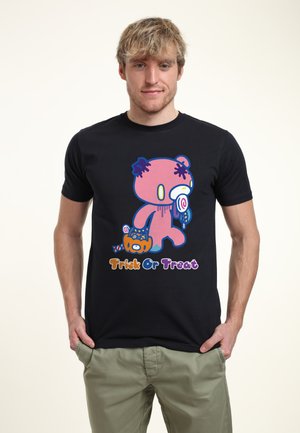 Ung mand iført sort t-shirt med tegneserie lyserød bjørn, der holder slik og græskarspand, tekst "Trick Or Treat" under designet.