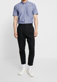 Korte mouwen, overhemd met knoopsluiting in lichtblauw chambray-stof, gecombineerd met zwarte geplooide broek en witte sneakers.