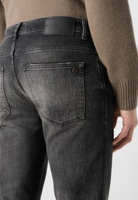 Jeans negri din denim cu un finisaj decolorat, având două buzunare la spate și o etichetă din piele neagră cu marca "BOSS" la talie.