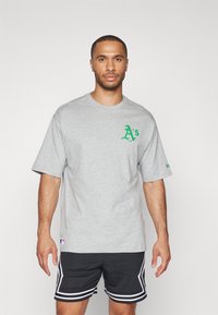 Camiseta gris de manga corta con un logo verde en el pecho. Fabricada en algodón, de corte relajado, con cuello redondo y dobladillos planos.
