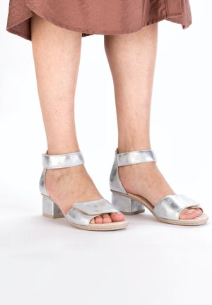 Sandales argentées à talons avec brides de cheville, design ouvert au niveau des orteils et texture métallique. Dotées d'un talon carré et d'une large bride à l'avant.