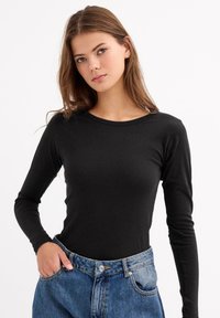 Top negro de manga larga con un escote redondo, hecho de una tela lisa; combinado con jeans de mezclilla azules de cintura alta.