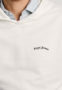 Felpa con cappuccio bianca in tessuto morbido con tasca anteriore. Presenta un logo "Pepe Jeans" curvo nero sul petto.