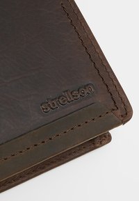 Bruine leren portemonnee met een gladde textuur, voorzien van een Strellson-logo dat op de buitenkant is geperst en contrasterende donkere stiksels langs de randen.