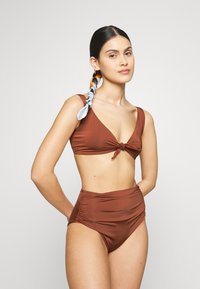Conjunto de bikini castanho com um top bralette com nó e com fundos de cintura alta com detalhes franzidos, feito de um tecido liso e elástico.