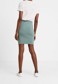 Une jupe moulante mi-cuisse vert menthe en tissu stretch, associée à un t-shirt blanc à rayures et des baskets blanches.