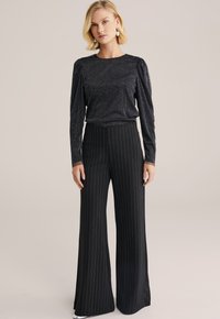 Top nero a maniche lunghe con scintillio metallico e spalle a sbuffo, abbinato a pantaloni larghi a righe verticali neri a vita alta.