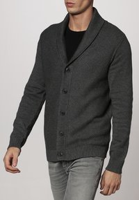 Mörkgrå stickad kofta med sjalkrage, med ett texturerat mönster och sex svarta knappar. Ribbad ärm- och nederkant.